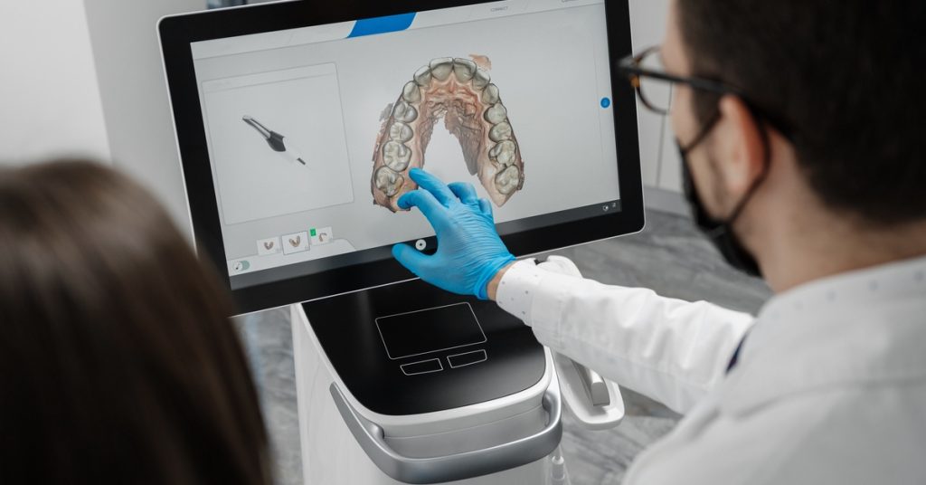 A dentist and someone else looking at a 3D scan of a set of teeth on the computer screen. The dentist is pointing at the screen.