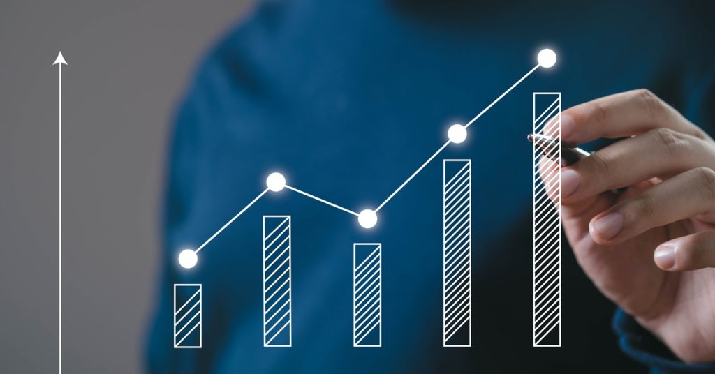 A person pointing a pen at a holographic bar graph. The graphic is floating in the air and has trend line connecting the bars.