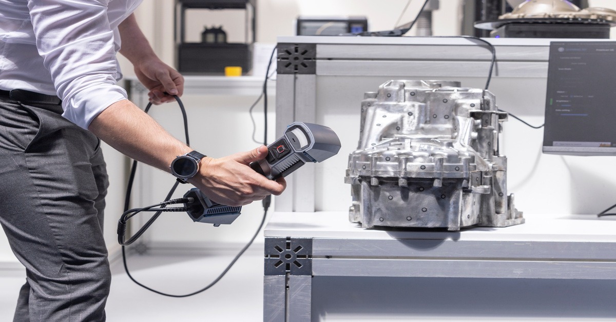 Someone using a 3D scanner to analyze an engine part. The person is in business attire and wearing a smartwatch.