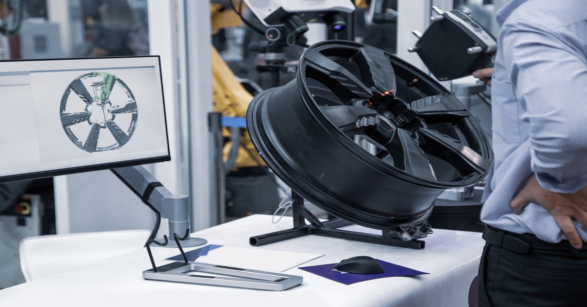 A person scanning a black rim with a 3D scanner. There is a computer screen that shows the scan so far.