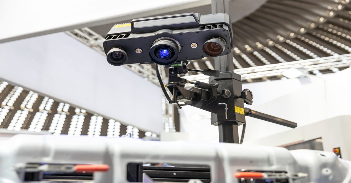 A 3D scanning camera facing downward, pointed as some car parts. The scanner has 3 camera lenses on it.