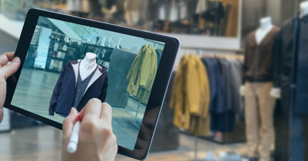 Someone using a stylus on a tablet that has a mannequin wearing a shirt and jacket. They are standing in a clothing store.