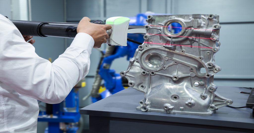 Someone positioning an arm with a 3D laser scanner in front of a large metal object. Red lines are running across the metal.