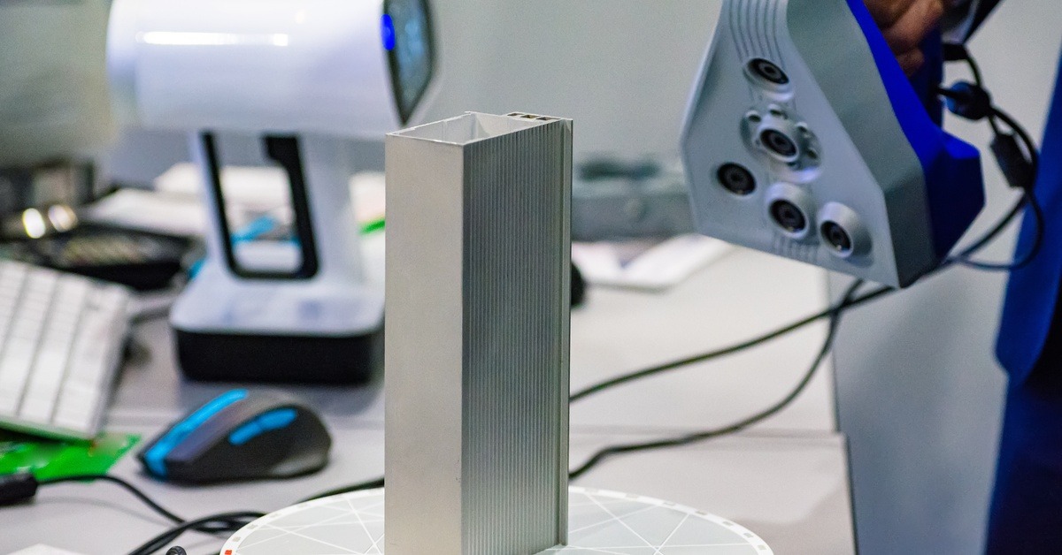 Someone using a 3D scanner on a rectangular piece of metal. The metal piece appears to be hollow in the middle.
