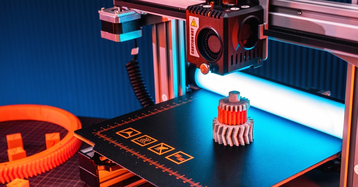 Some gears sitting on top of each other on a 3D printer. The middle one is red and the other two are gray.